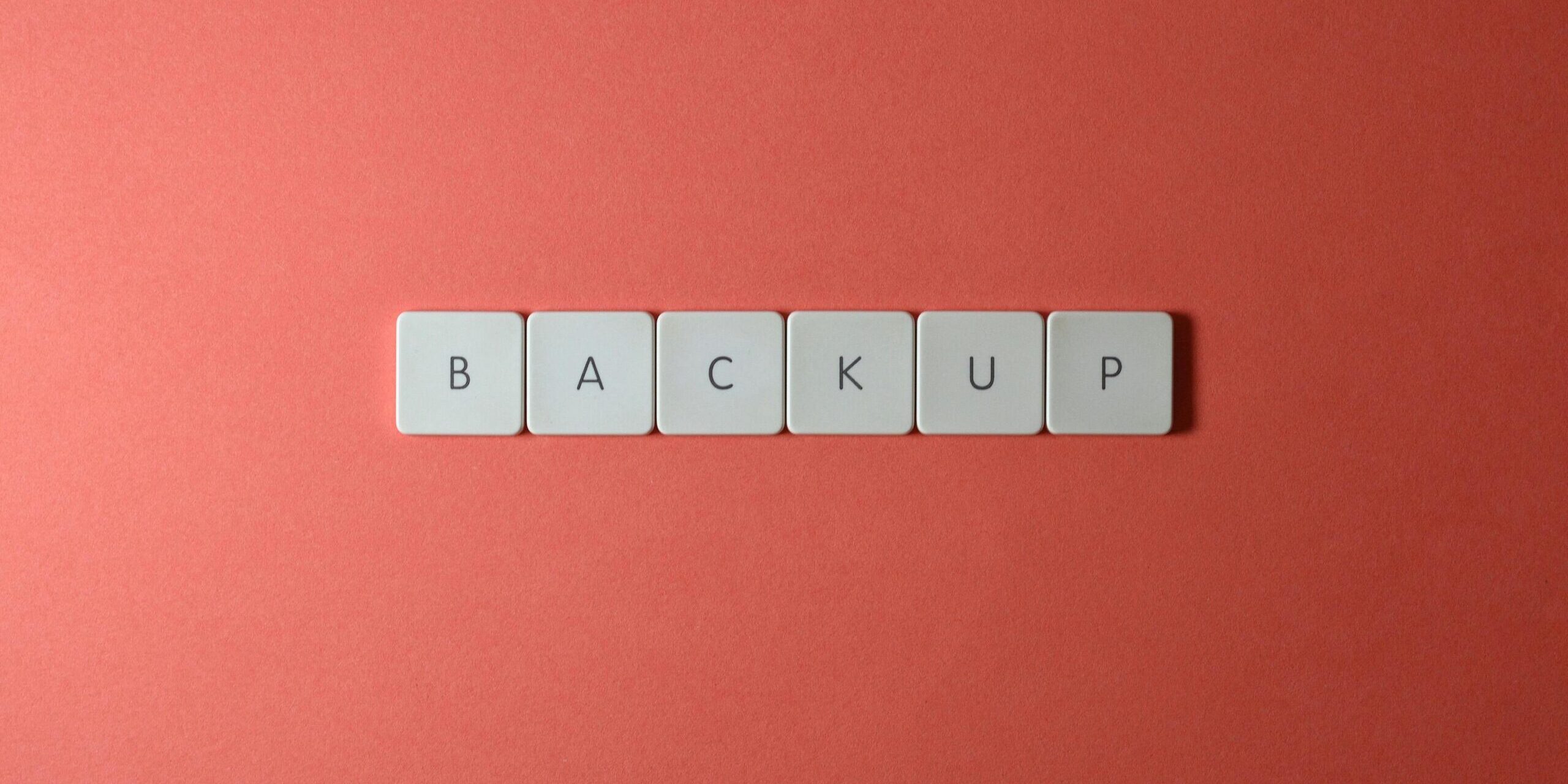 Simple-Backup-and-Recovery-Plans-Every-Small-Business-Needs-scaled.jpg Free Close-up of keyboard keys spelling 'BACKUP' placed on a coral-colored surface. Stock Photo