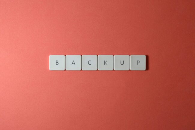 Simple-Backup-and-Recovery-Plans-Every-Small-Business-Needs-scaled.jpg Free Close-up of keyboard keys spelling 'BACKUP' placed on a coral-colored surface. Stock Photo
