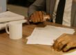 Free Close-up of a businessman holding and reviewing documents on a wooden desk. Stock Photo