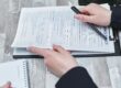 Free Close-up of hands analyzing insurance policy paperwork with pen on table. Stock Photo